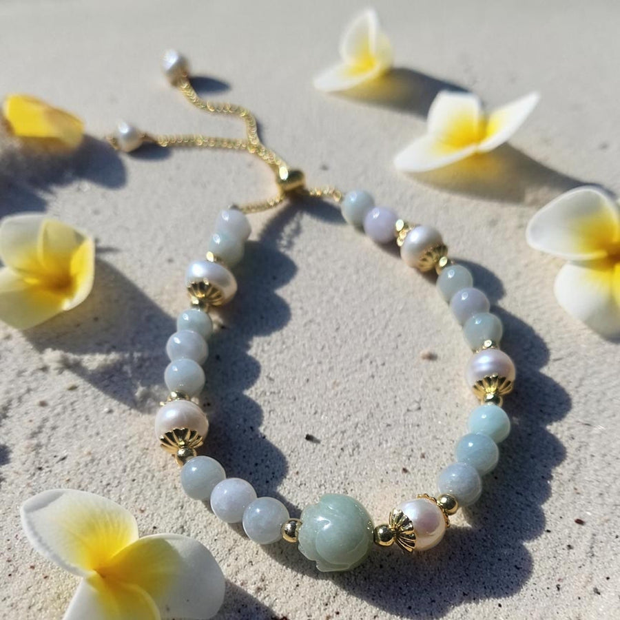 Beaded natural Jade bracelet with gold accents on a sandy surface with flowers