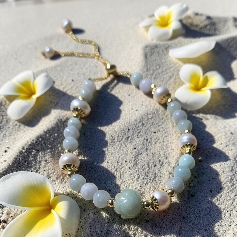 Natural Jade Tulip bracelet with pearls and gold accents on a sandy beach with  plumeria flowers.