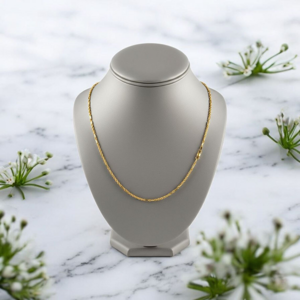 Gold necklace on a gray bust with a marble background and greenery